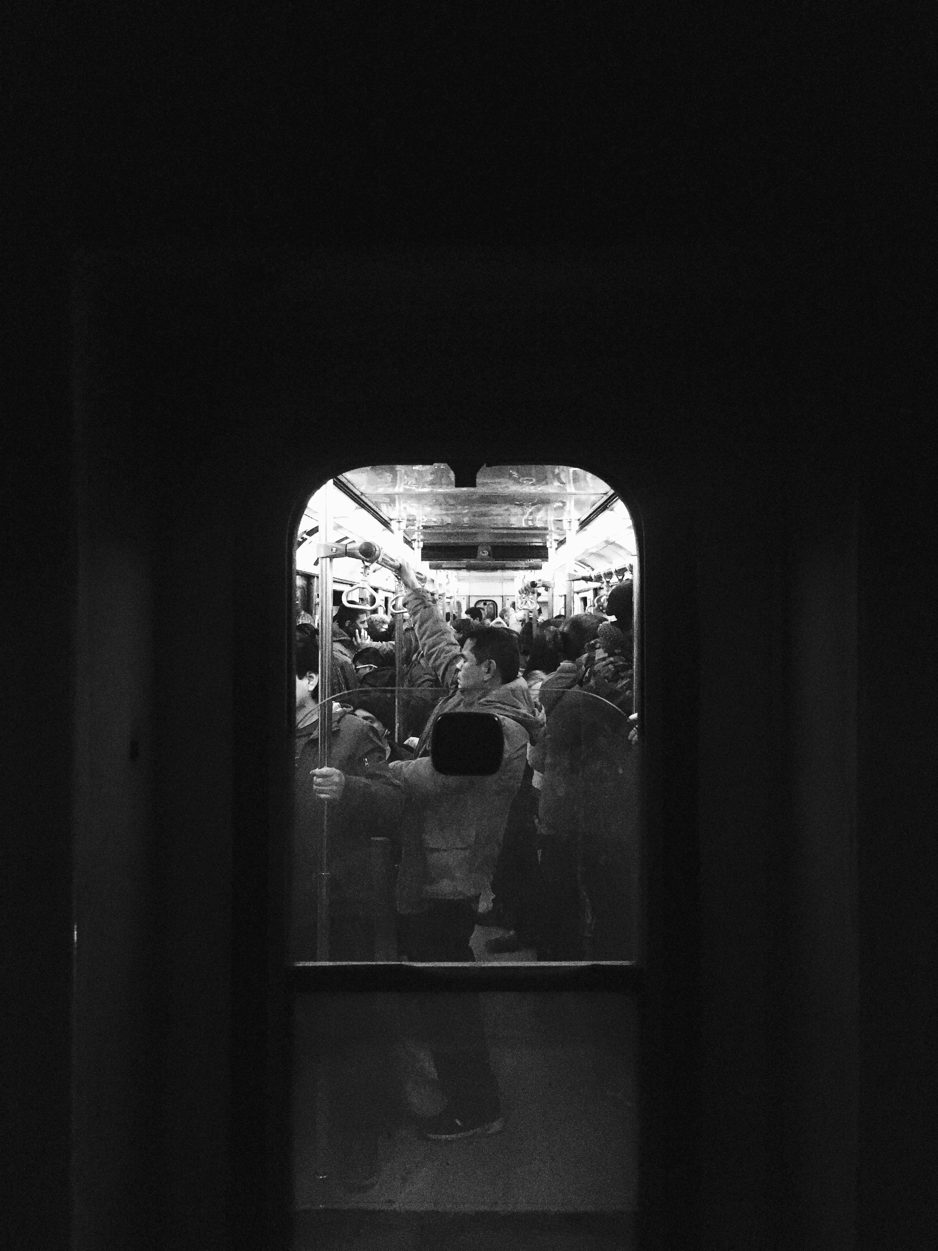 Nostalgic, black and white image of a man inside Santiago's subway. The picture is captured from a different subway car, and the small window of the man's car acts as an artificial frame for his body. The man's eyes are closed, and his body language seems to convey sadness, or tiredness.